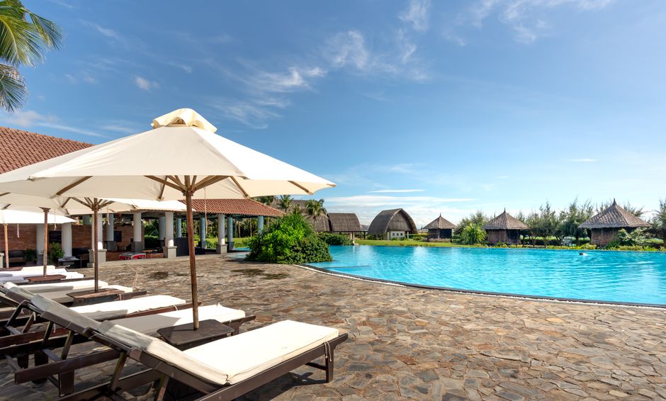 Scenic view of a luxury resort pool with sunbeds and umbrellas under a clear sky.