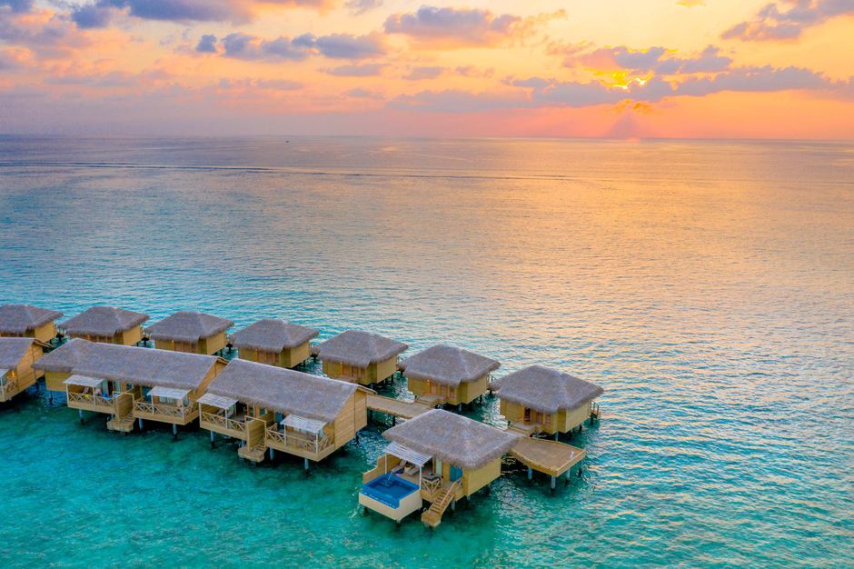 Aerial view of stunning overwater villas with a vibrant sunset over a tropical ocean.